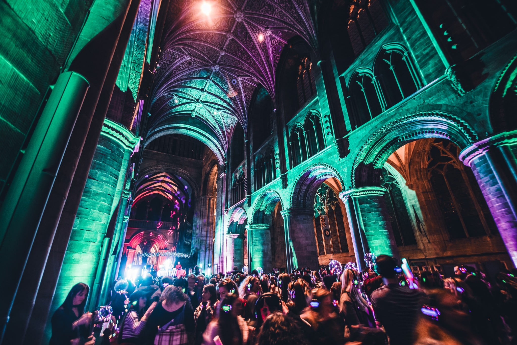 Grote groep personen heeft een silent disco in een kerk met verschillende veel kleuren lichten.